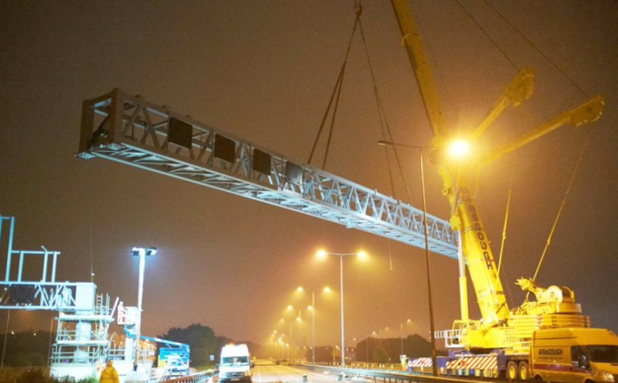 A crane moving a motorway overhead gantry into position at night
